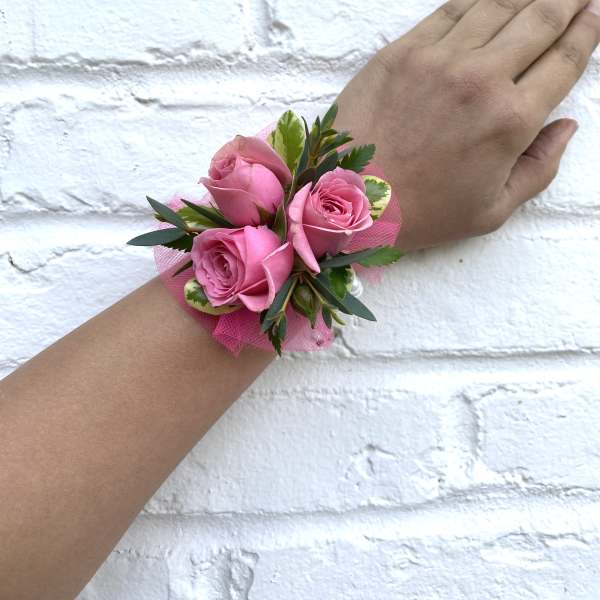 Pink rose wrist corsage with green foliage on a hand