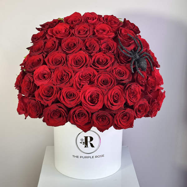 Large dome of red roses in a white hatbox with a black decorative spider on one side.