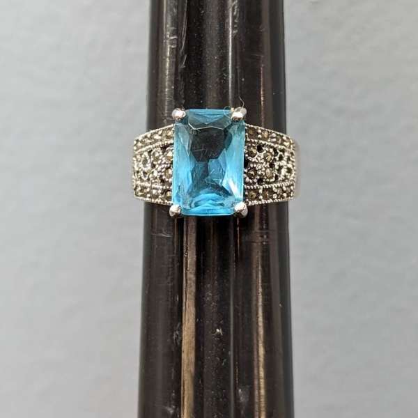 Silver ring with a rectangular blue gemstone on a dark stand