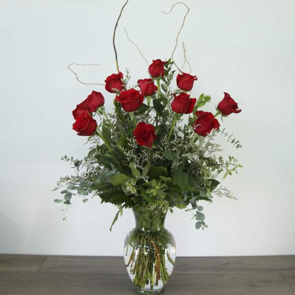 Red roses arranged in a clear glass vase with greenery