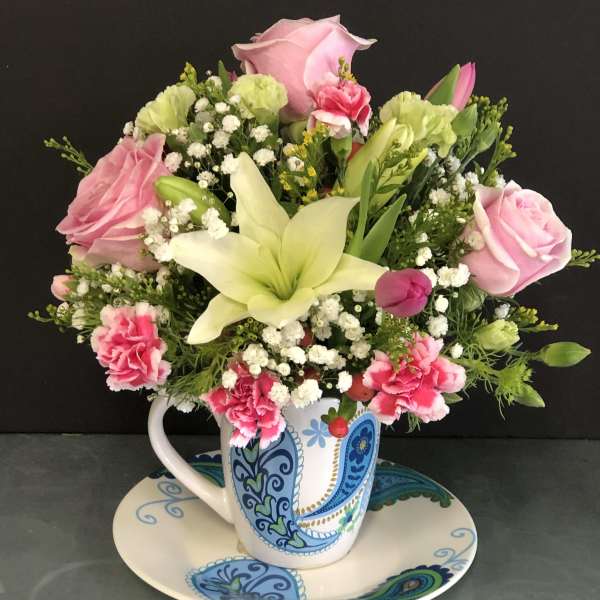 Pink roses and lilies arranged in a patterned mug on a matching saucer