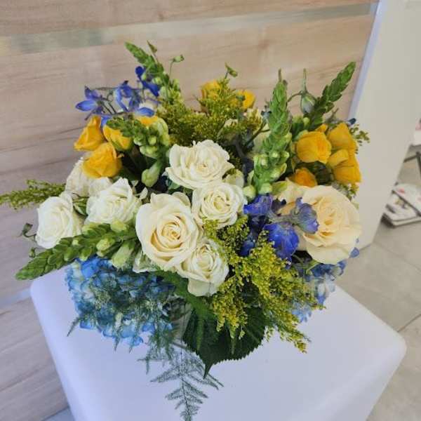 Round arrangement of cream roses, yellow blooms and blue flowers in a compact mixed bouquet