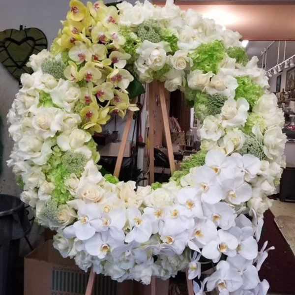 Large white floral wreath on a wooden stand with cascading orchids