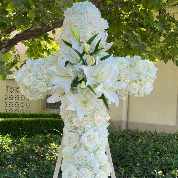 White floral cross on a wooden easel with roses and lilies