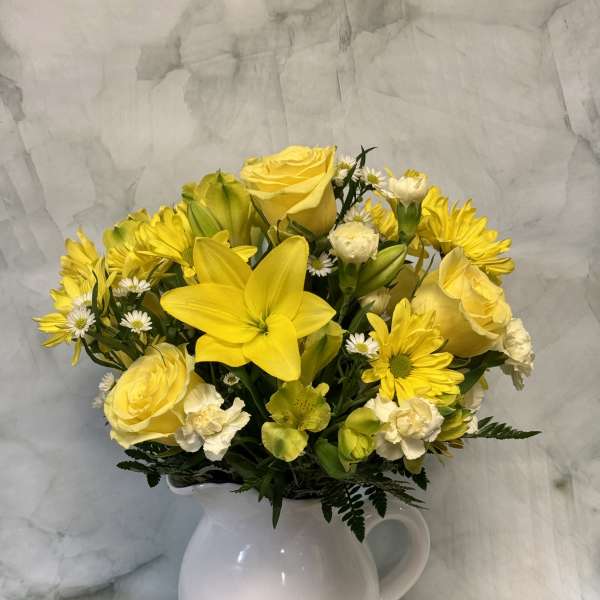 Yellow flowers arranged in a white pitcher vase