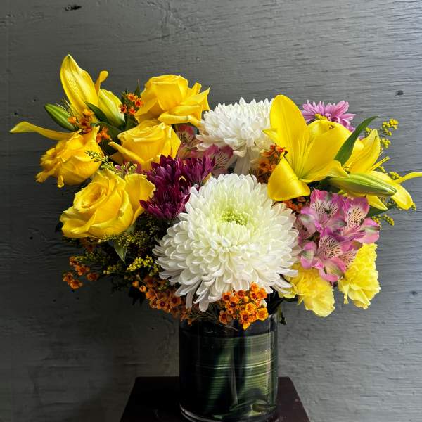 Bouquet of yellow roses, white chrysanthemums, and lilies in a glass vase