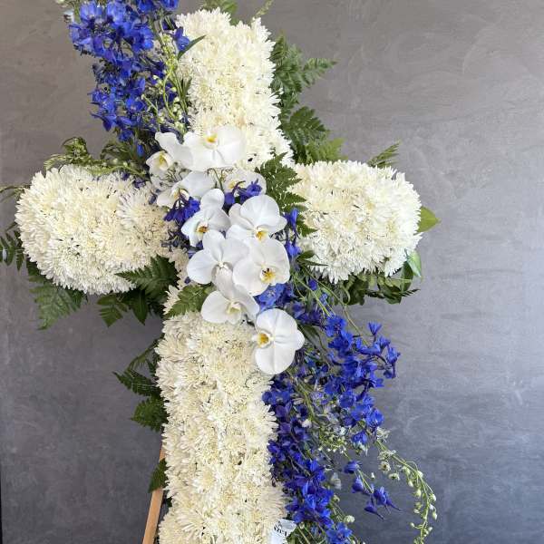Standing floral cross with white chrysanthemums, white orchids, and blue delphinium
