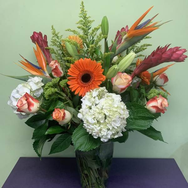 Tropical bouquet with orange gerbera daisies, roses, and white hydrangeas in a glass vase