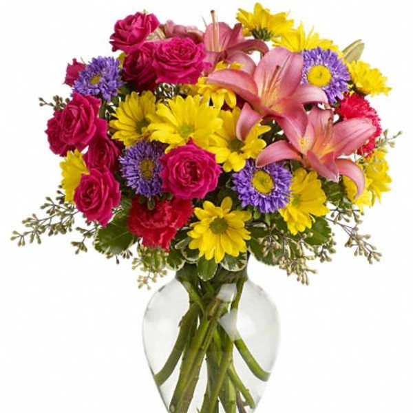 Bouquet of pink roses, lilies, and yellow daisies in a clear glass vase