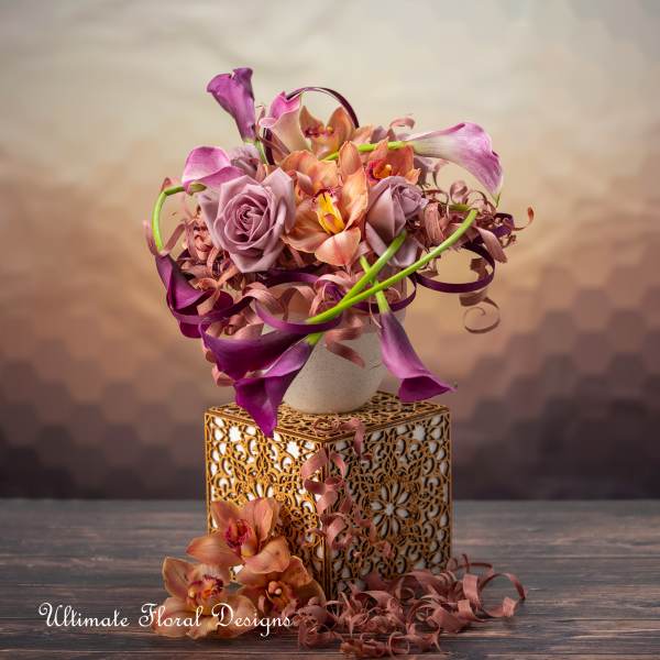 Purple calla lilies and roses arranged in a decorative vase on a gold stand