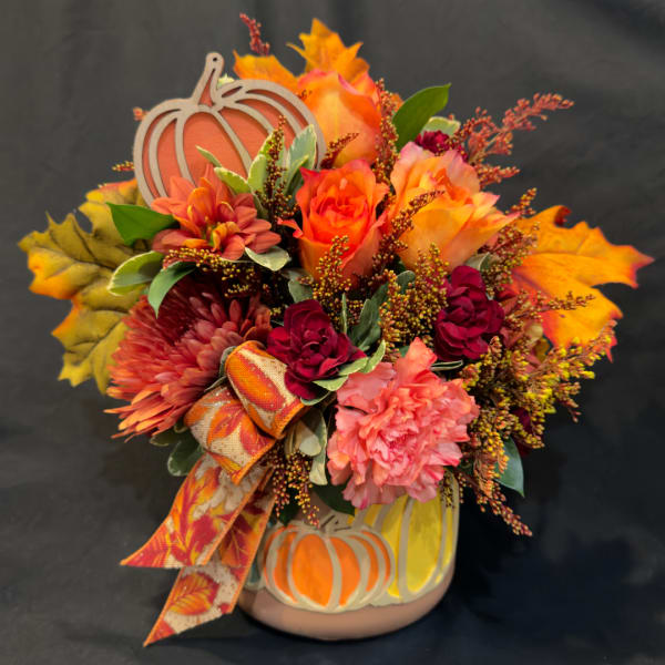 Autumn floral arrangement in a pumpkin vase with orange, pink, and burgundy blooms