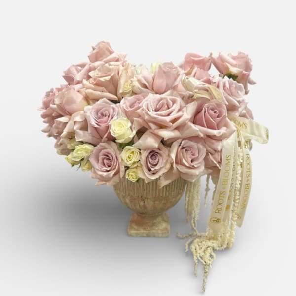 Blush pink roses arranged in a pedestal vase with a ribbon accent