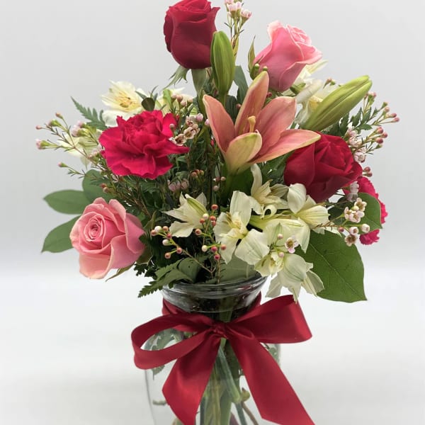 Mixed bouquet of roses, lilies, and carnations in a glass vase with a red ribbon