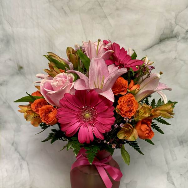 Pink and orange mixed flower arrangement in a vase with a ribbon