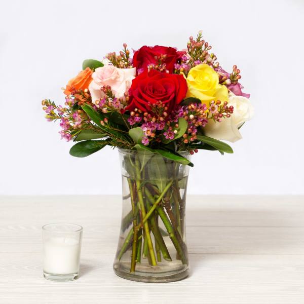 Mixed roses in a clear glass vase with a small candle beside it