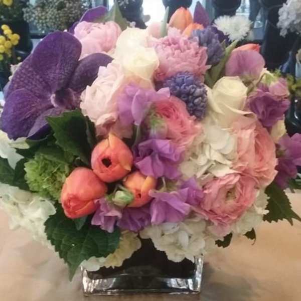 Mixed bouquet of pink, purple, and white flowers in a square glass vase