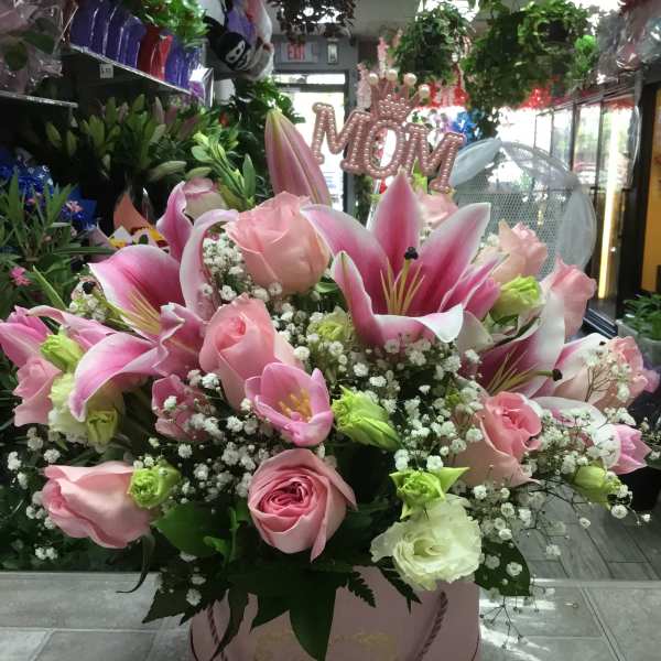Pink lilies and roses arranged in a round pink box.