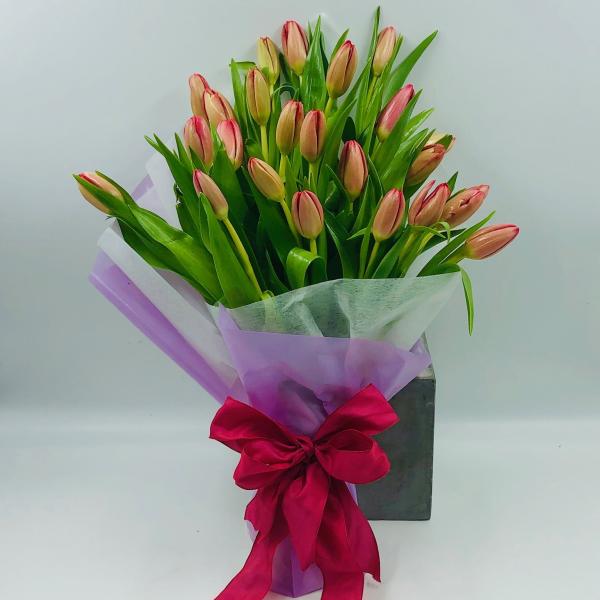 Bouquet of pink tulips wrapped in purple paper with a red ribbon