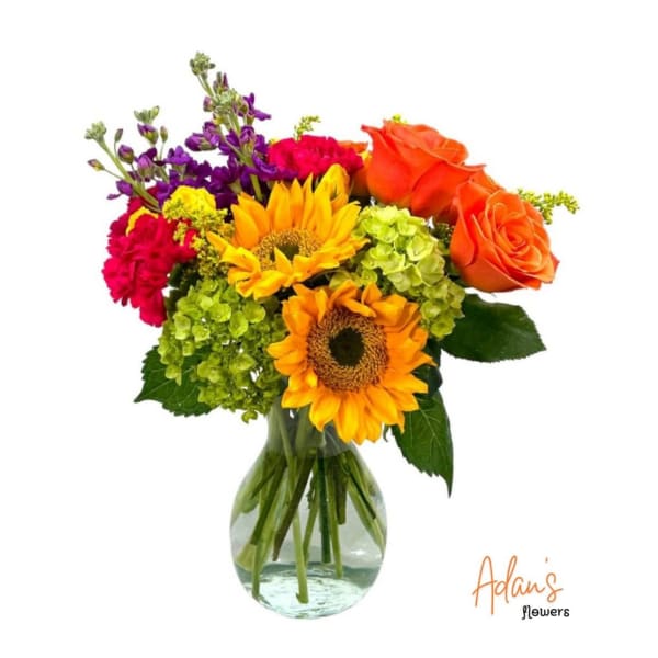 Mixed bouquet with sunflowers, orange roses, purple flowers, and green hydrangeas in a glass vase