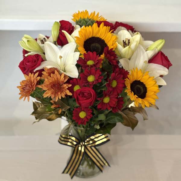 Mixed bouquet of sunflowers, lilies, roses, and daisies in a glass vase