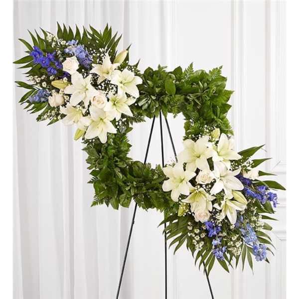 Heart-shaped floral wreath with white lilies and blue flowers on a stand
