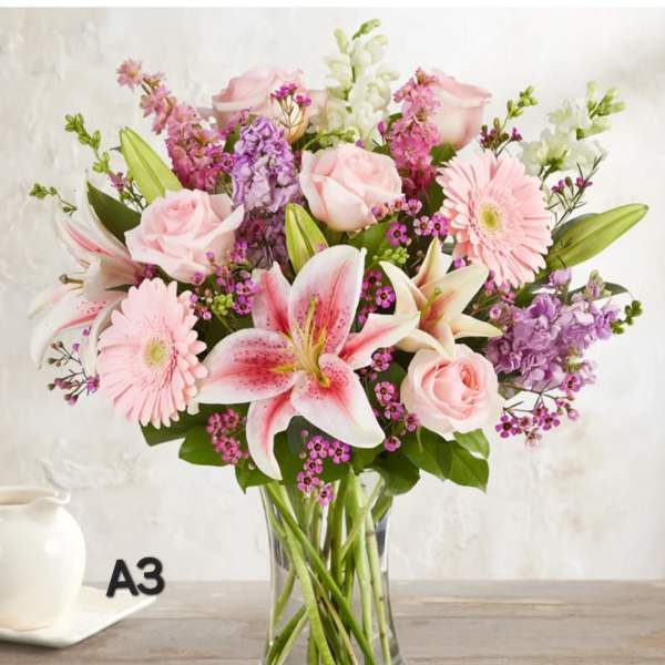 Pink roses and lilies arranged with gerberas in a clear glass vase