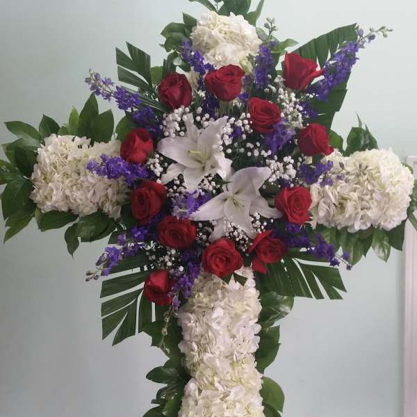 Cross-shaped floral arrangement with red roses, white lilies, and white hydrangeas