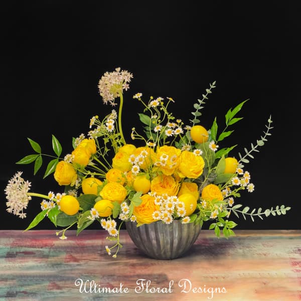 Yellow roses and daisies arranged in a metal bowl with lemon accents