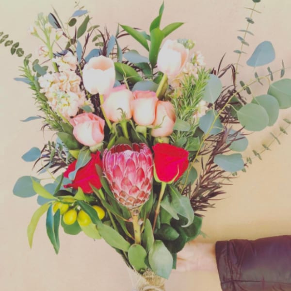 Handheld bouquet with pink roses, a protea, and pale tulips