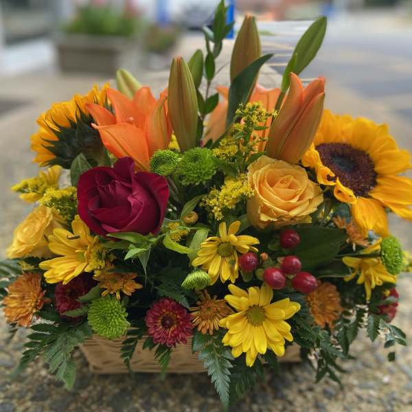 Mixed bouquet with sunflowers, roses, lilies, and daisies in a basket