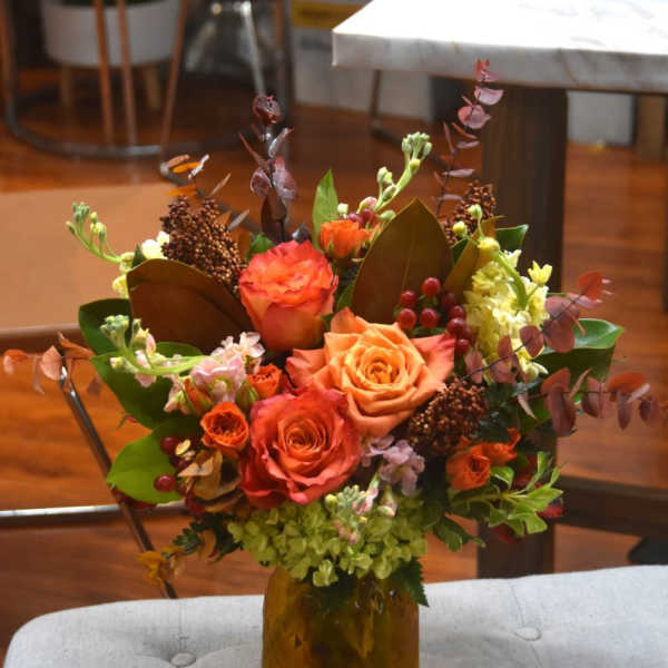 Autumn-toned bouquet of orange roses and mixed blooms in an amber glass jar vase