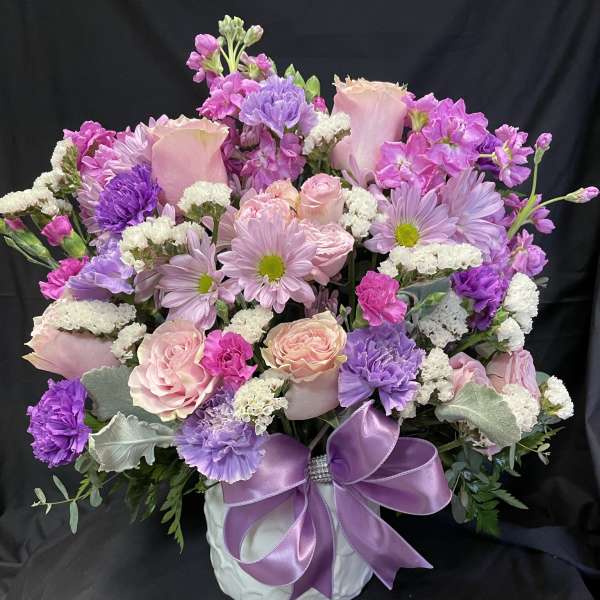 Pink and purple mixed bouquet in a white vase with a lavender ribbon