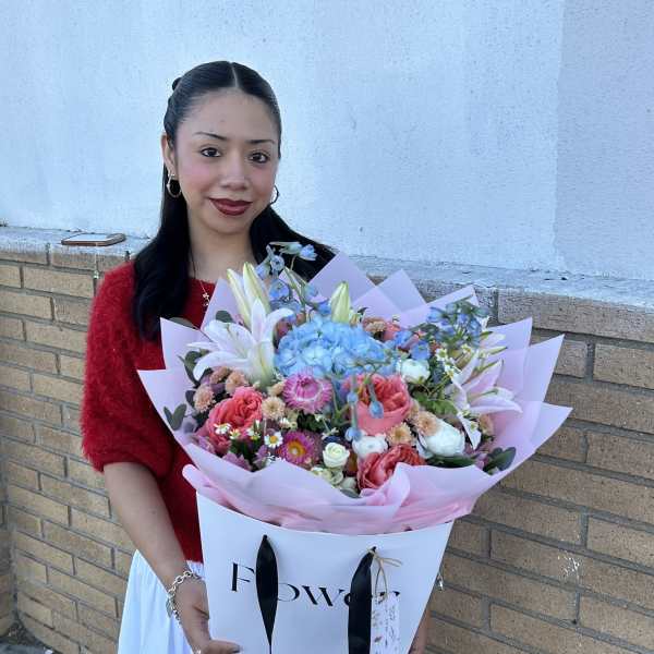 Woman holding a large pastel bouquet with lilies, roses, and blue hydrangeas