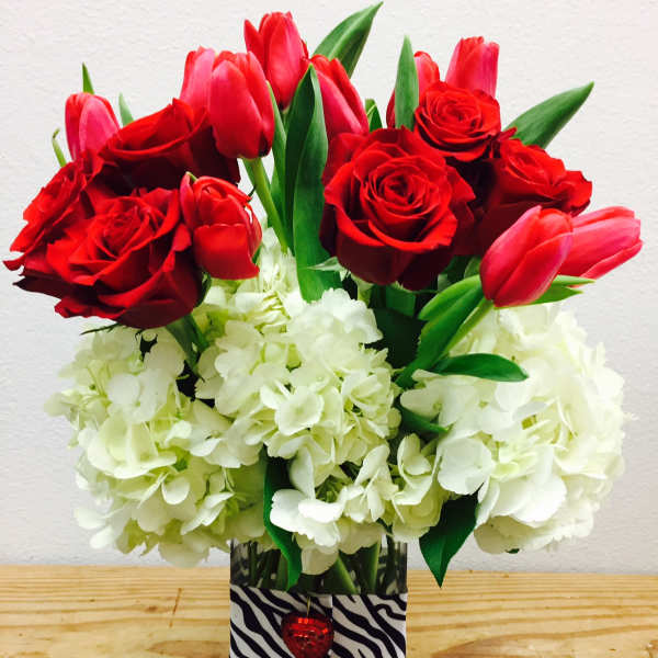 Red roses and pink tulips in a glass vase with white hydrangeas