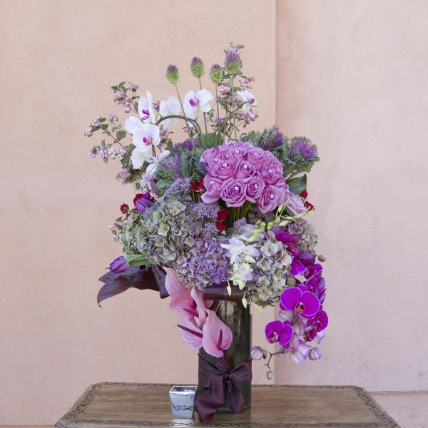 Tall bouquet of pink roses, orchids, and hydrangeas in a glass vase