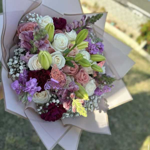 Hand-tied bouquet of pink, white, and purple flowers wrapped in pale paper