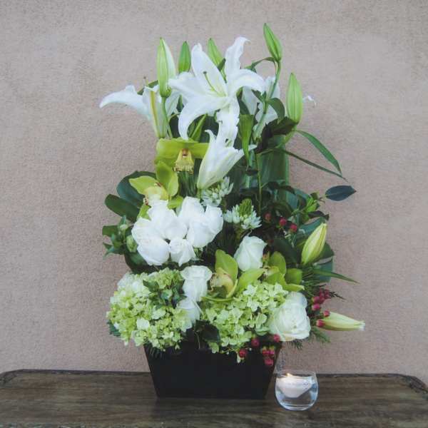 White lilies and green blooms in a black container beside a candle