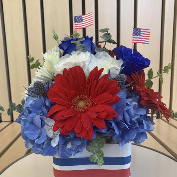 Red, white, and blue flower arrangement in a white box with small American flags