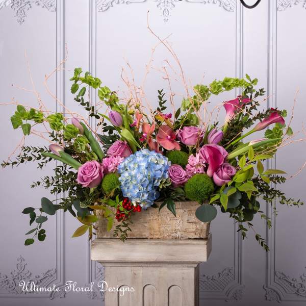 Large floral arrangement with pink roses, blue hydrangea, and calla lilies in a stone container