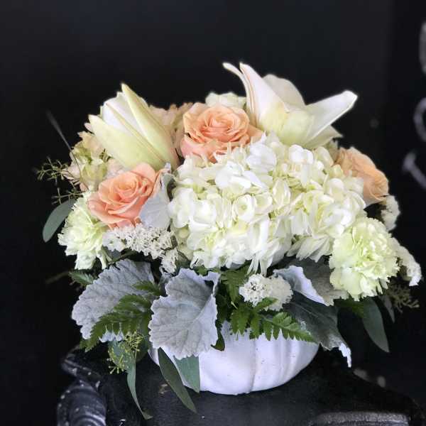 Peach roses and white lilies arranged in a white vase