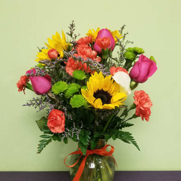 Mixed bouquet with sunflowers, pink roses, carnations, and a glass vase