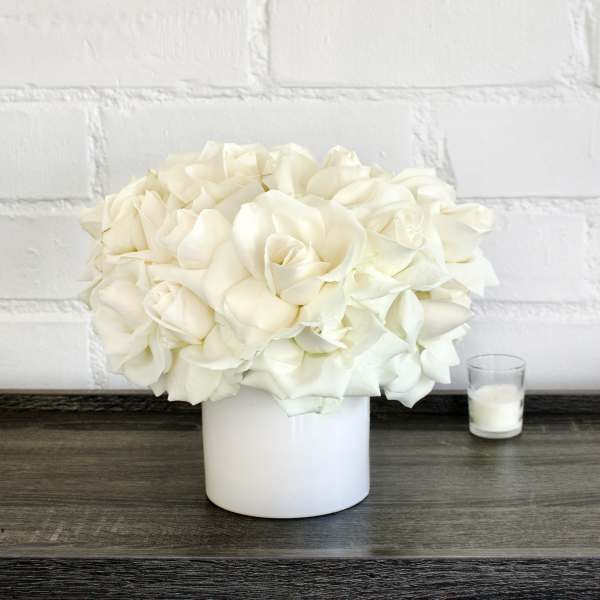 White rose bouquet in a white vase beside a small candle