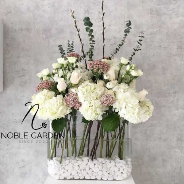 White floral arrangement in a clear rectangular vase with tall branches