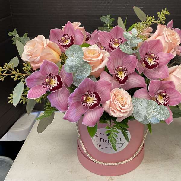 Pink orchids and peach roses arranged in a pink hatbox
