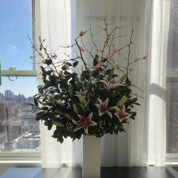 Tall floral arrangement with pink lilies and flowering branches in a white pedestal vase