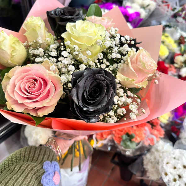 Hand-tied bouquet of pink, cream, and black roses with white filler flowers in pink wrap