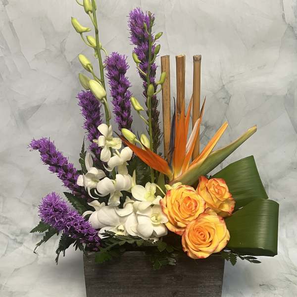 Tropical floral arrangement with orange roses, white orchids, and purple spikes in a wooden box