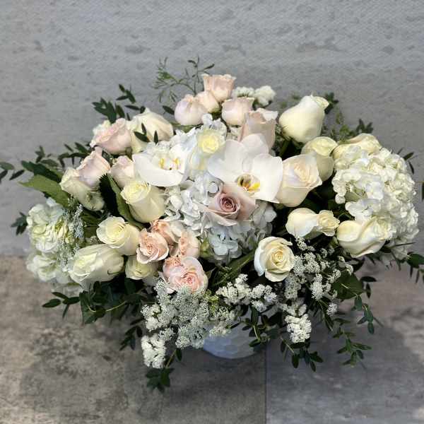 Low bouquet of white and blush roses with white orchids in a vase