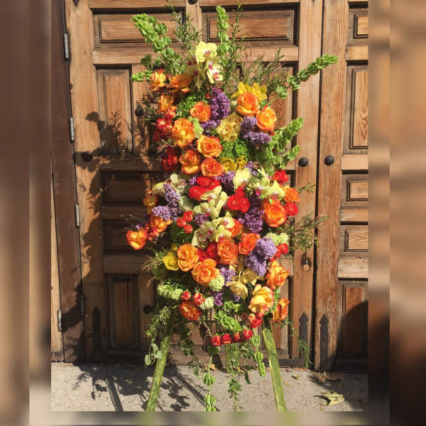 Tall floral standing spray on an easel with orange, yellow, red, and purple blooms