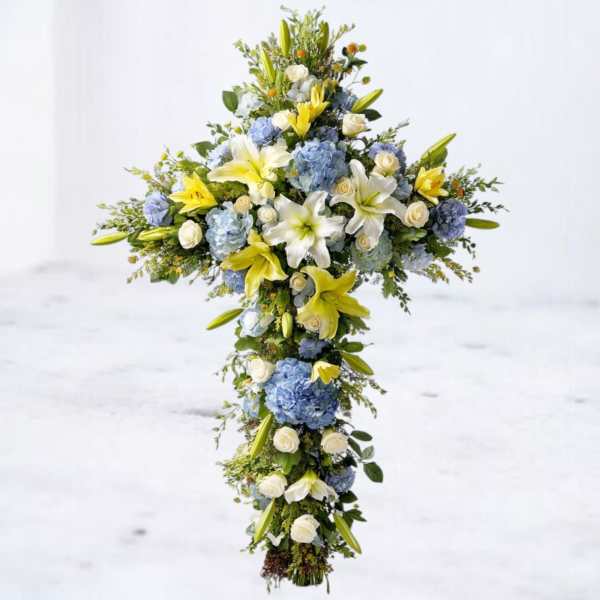 Tall floral cross with white lilies, blue hydrangeas, and white roses